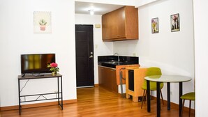 A compact kitchen with a black door, wooden cabinets, a small dining table with two chairs, and a TV on a stand. - The Boni Tower By Rspl (Mandaluyong)