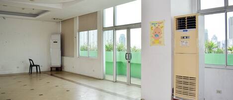 Ένα ευρύχωρο δωμάτιο με μεγάλα παράθυρα, έναν ανεμιστήρα θέρμανσης και μια αφίσα στον τοίχο.