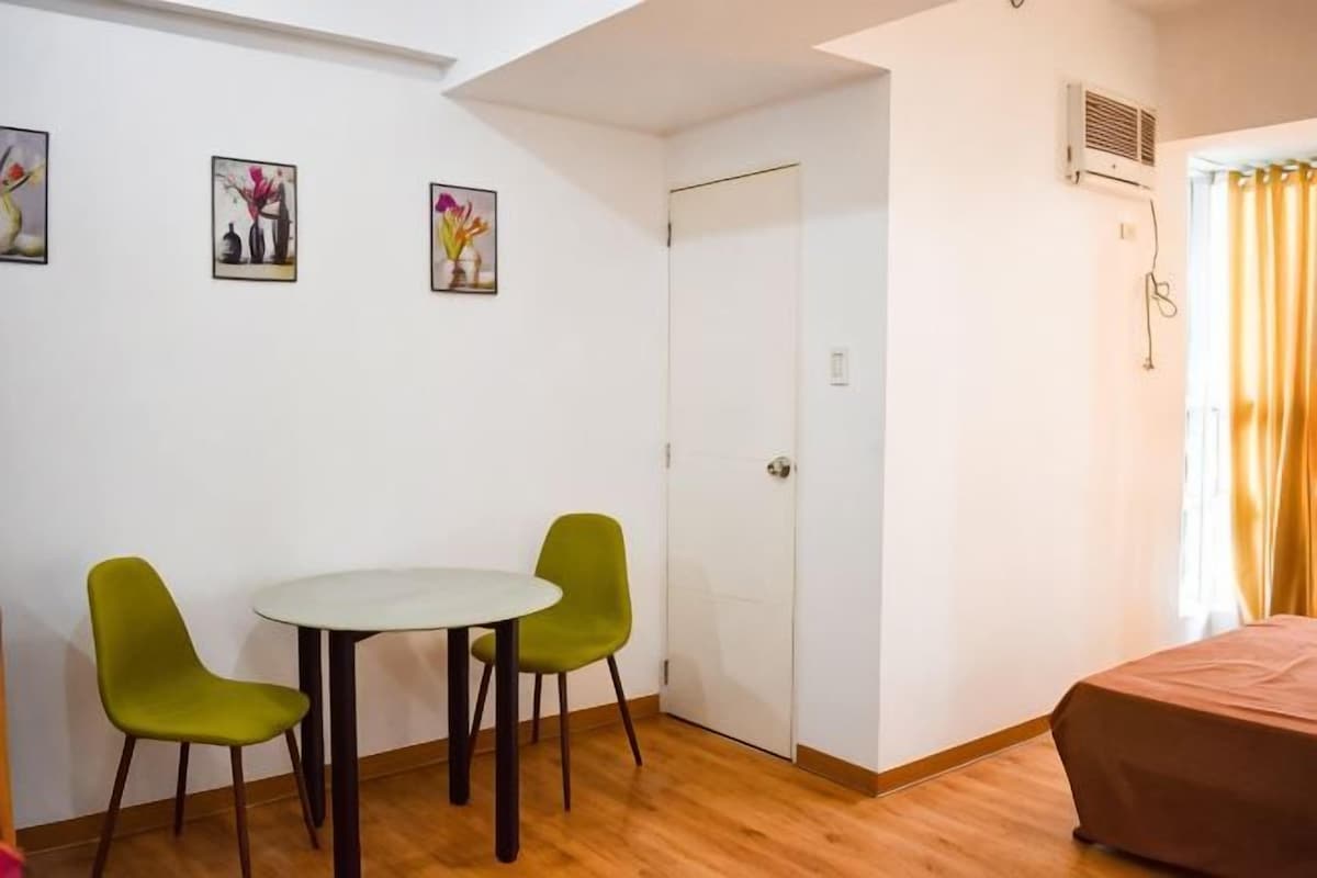 A room with a bed, a table with two chairs, a door, and three framed pictures on the wall.
