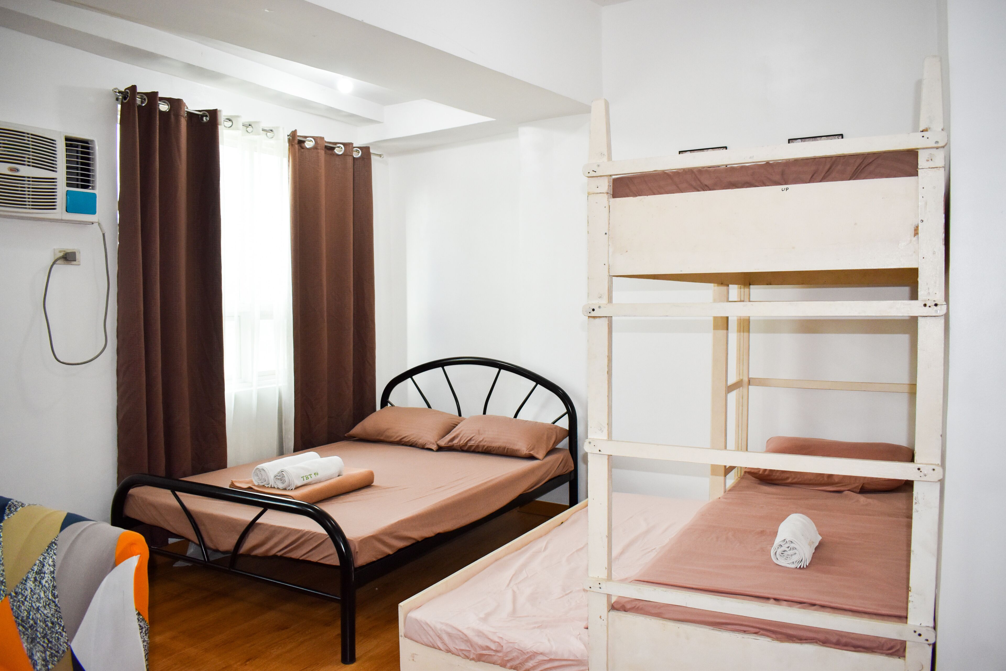 A dormitory room with a single bed, a bunk bed, a window with curtains, and an air conditioning unit.