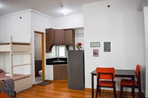 A compact room with a bunk bed, kitchenette, dining table with chairs, and a refrigerator. - The Boni Tower By Rspl (Mandaluyong)