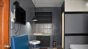 A compact room with a kitchenette, a single bed, a blue cushioned bench, and a small round table with a chair. - 1812 Vc Lodge (Manila)