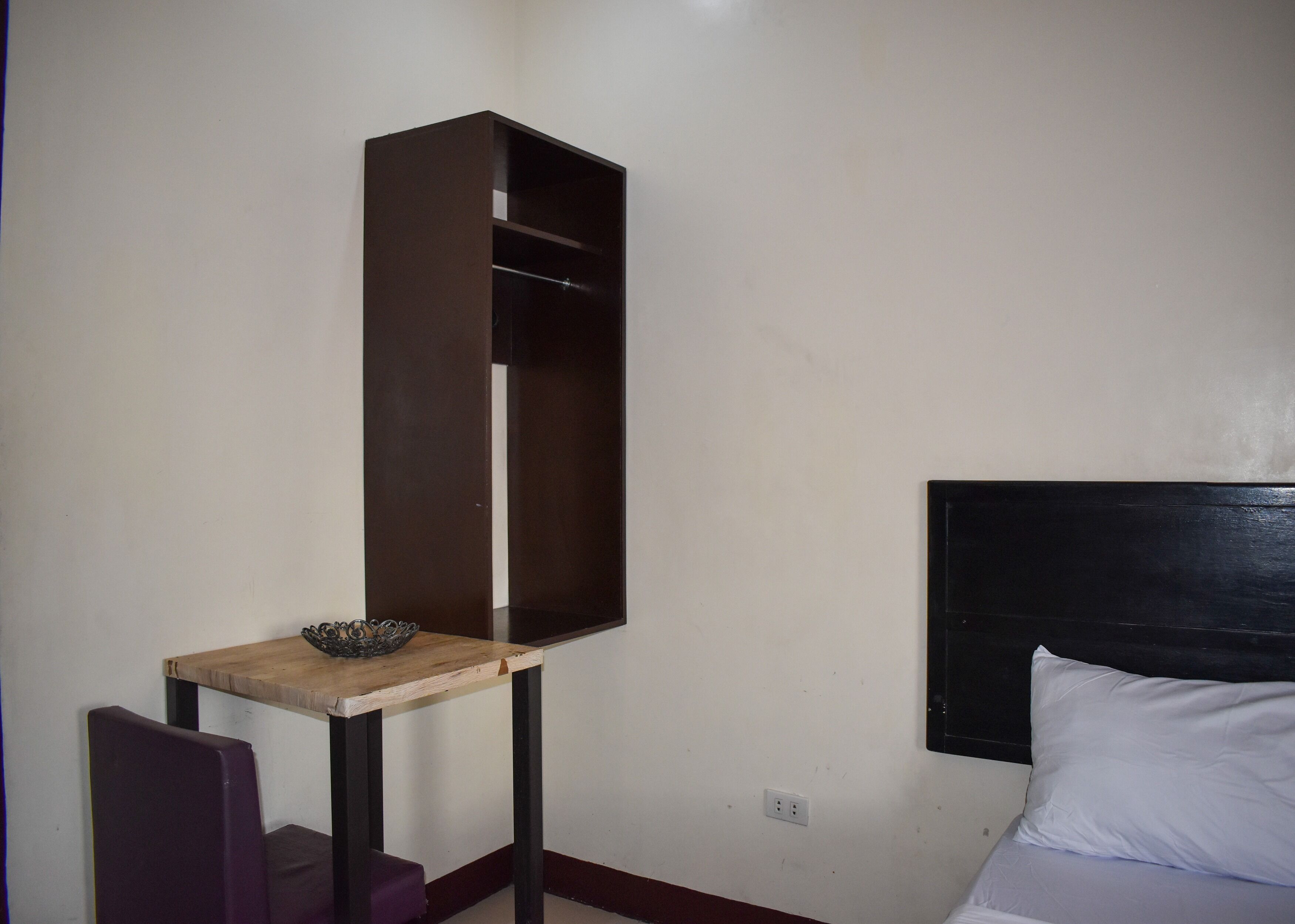 A room with a bed, a wooden nightstand, a dark-colored wardrobe, and a wall socket.
