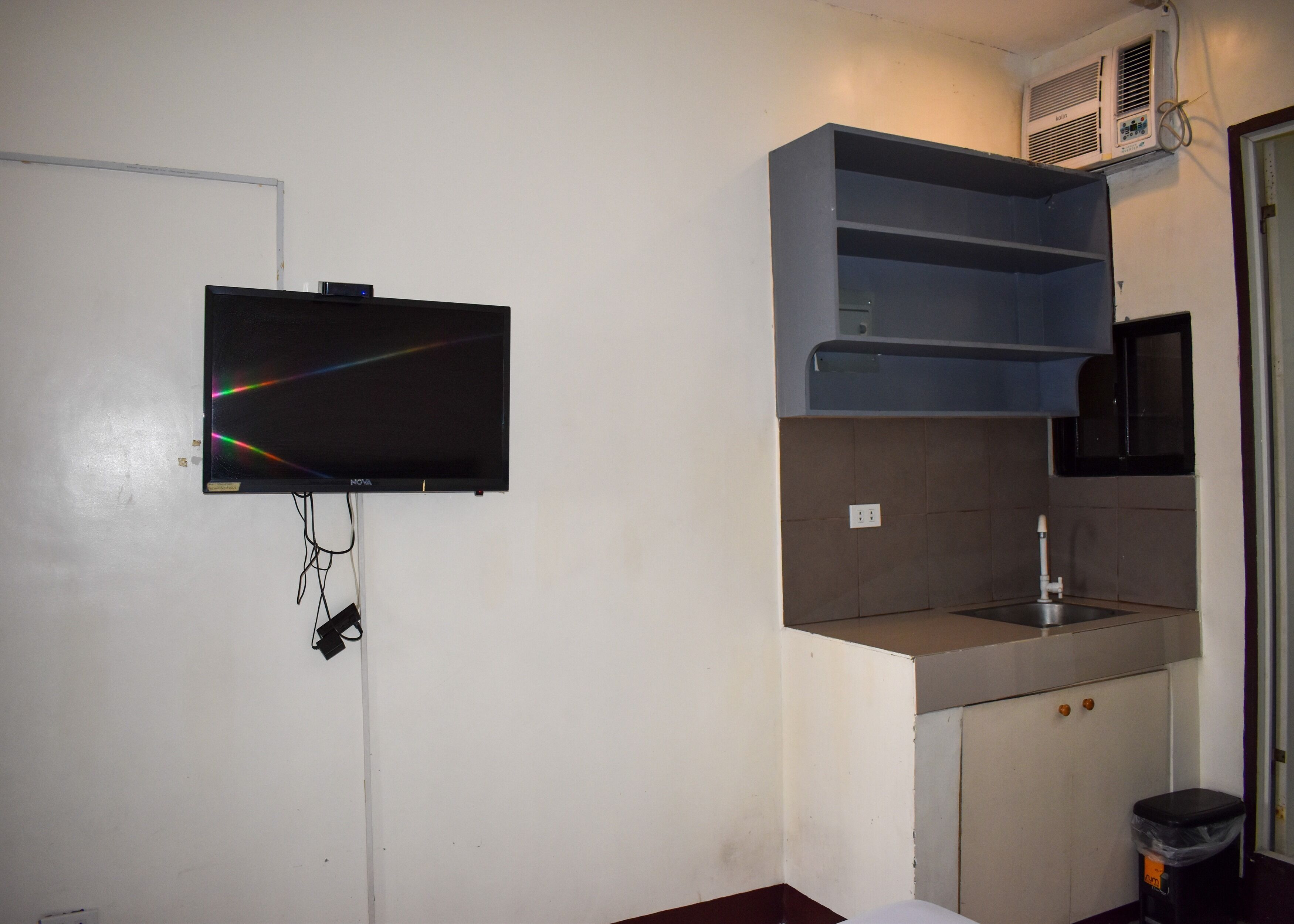 Una pequeña kitchenette con un lavamanos, un microondas y un televisor montado en la pared.