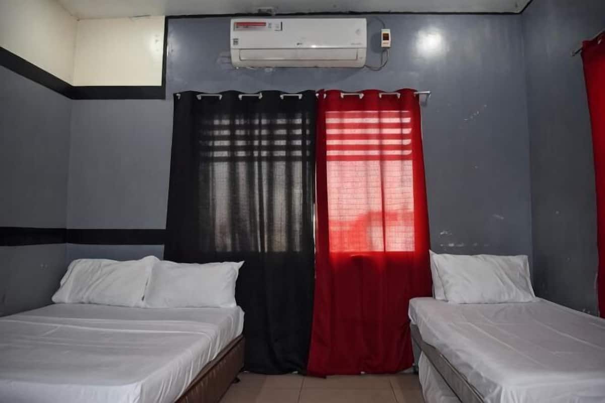 A room with two beds, a window with red curtains, and an air conditioning unit.