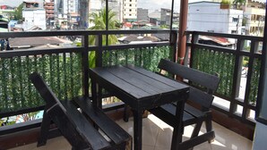 A balcony with a wooden table and benches, offering a view of a cityscape with buildings and a street. - 1812 Vc Lodge (Manila)
