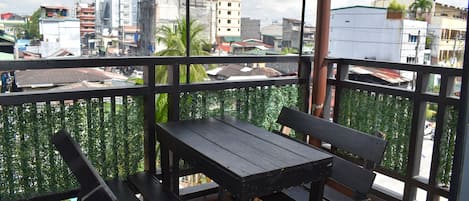 A balcony with a wooden table and benches, offering a view of a cityscape with buildings and a street.