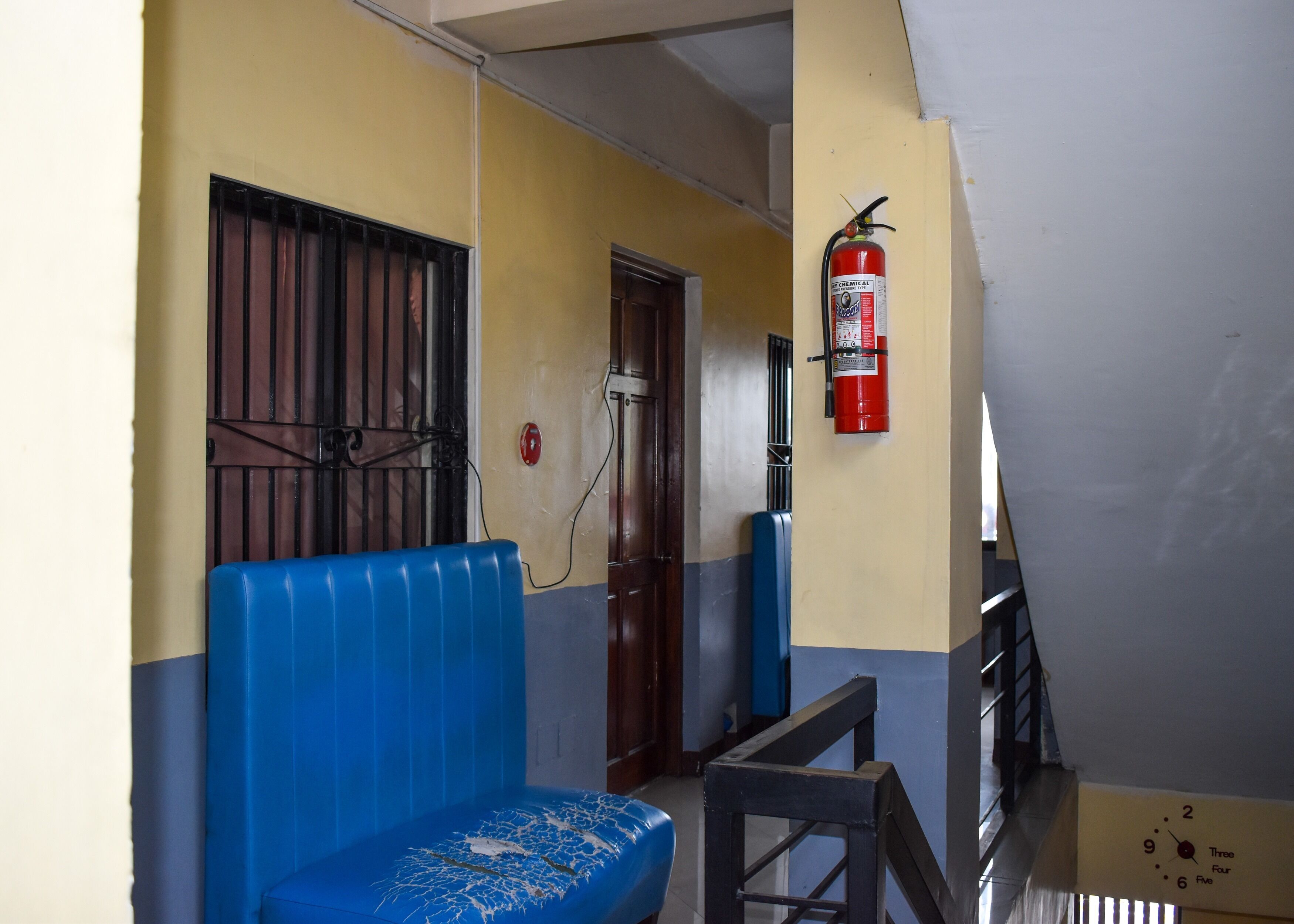 Un couloir avec un banc bleu, un extincteur et une porte dotée d’un portail en métal.