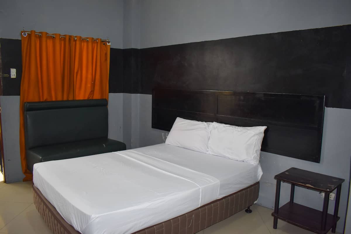 A single bed with a headboard, a small bedside table, and an orange curtain.