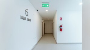 Un couloir avec un extincteur, un panneau indiquant la sortie et des panneaux indiquant le numéro des pièces.