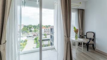 Una habitación con un ventanal grande, una silla, una mesita y un equipo de aire acondicionado.