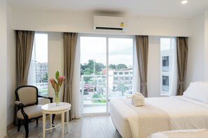 A hotel room with a bed, a chair, a small table with flowers, and a view of the city through large windows.