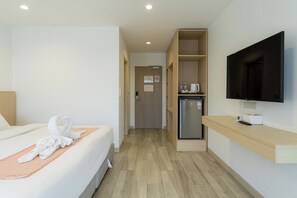 Habitación de hotel con cama, televisor, minibar y puerta que da a una kitchenette.