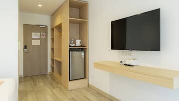 A modern hotel room with a built-in wooden shelving unit, a flat-screen TV mounted on the wall, and a built-in refrigerator.
