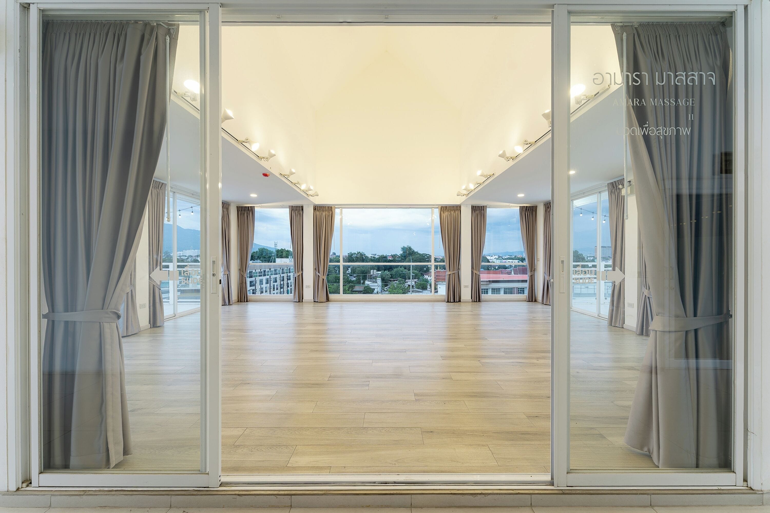 Una habitación amplia con ventanas grandes, suelo de madera y cortinas.