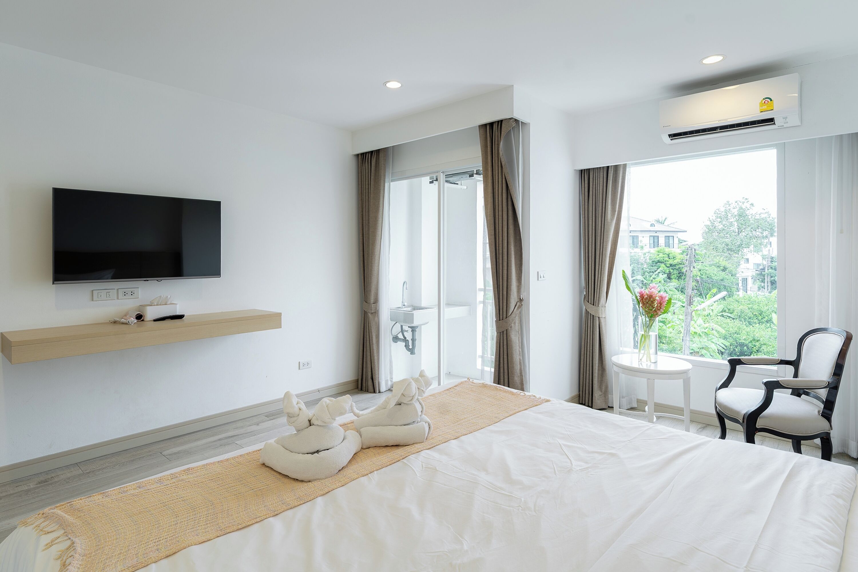A hotel room with a bed, a TV, a sink, a shower, a chair, and a view of the outdoors.
