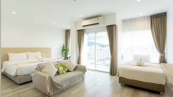 Habitación de hotel con dos camas, un sofá, un ventanal grande con cortinas, un aire acondicionado y una planta.