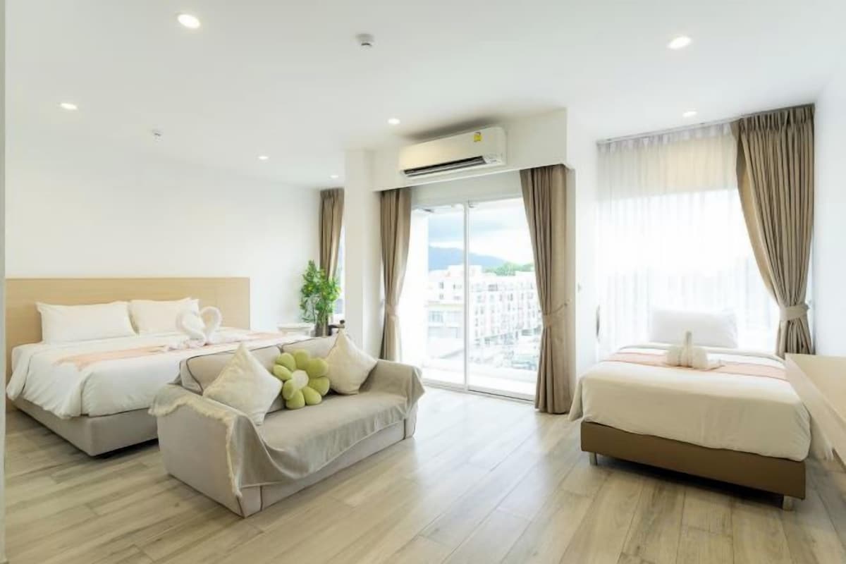 Habitación de hotel con dos camas, un sofá y un ventanal con cortinas.