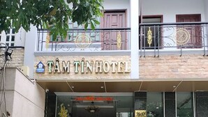 De ingang van Tam Tin Hotel met een trap die naar de ingang leidt, een bord boven de ingang en een potplant aan de rechterkant.