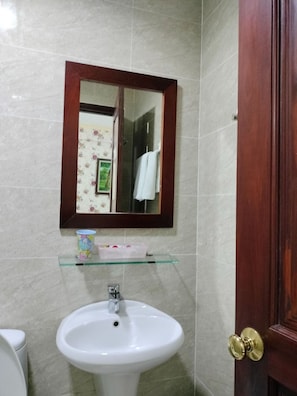 A bathroom with a white sink, a mirror with a wooden frame, and a glass shelf with toiletries. - Tam Tin Hotel (Ho Chi Minh City)