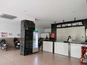 Un espace d’accueil d’hôtel avec un comptoir en marbre, un réfrigérateur et des scooters garés.