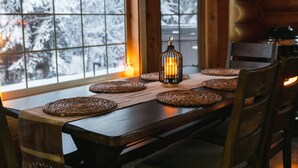 Uma mesa de jantar de madeira com jogos americanos trançados, uma vela e um candeeiro.