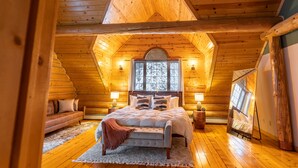 Quarto de cabana de toras aconchegante, com uma cama grande, um sofá e um espelho refletindo o ambiente.