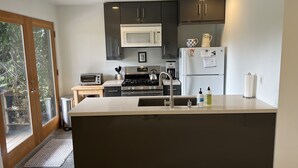 A modern kitchen with dark cabinets, a white countertop, a built-in microwave, a refrigerator, a stove, and a sink. - Garden apt. above the beach close to hiking trails and beach. (Stinson Beach)