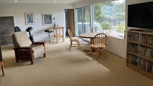 A modern living room with a treadmill, exercise bike, and a large TV. There are two wooden chairs and a small table with a plant. - Garden apt. above the beach close to hiking trails and beach. (Stinson Beach)