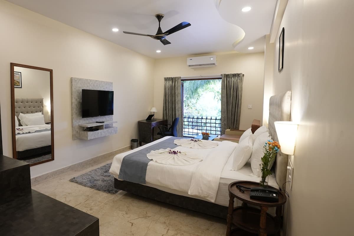 A modern hotel bedroom with a large bed, a flat-screen TV, a ceiling fan, and an air conditioning unit.