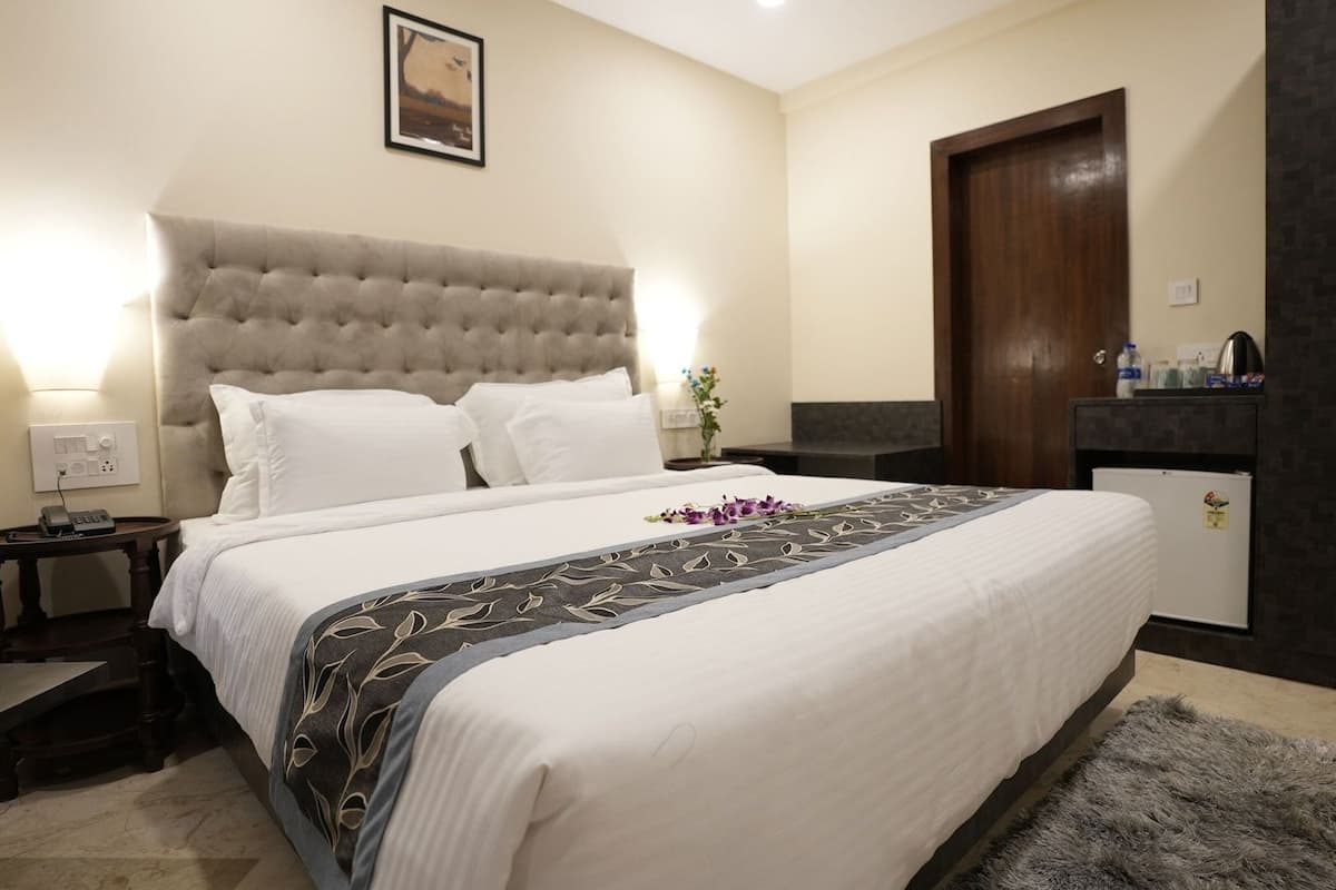A hotel room with a large bed, a wooden nightstand, a desk, a dark-colored wardrobe, and a small table with a vase of flowers.