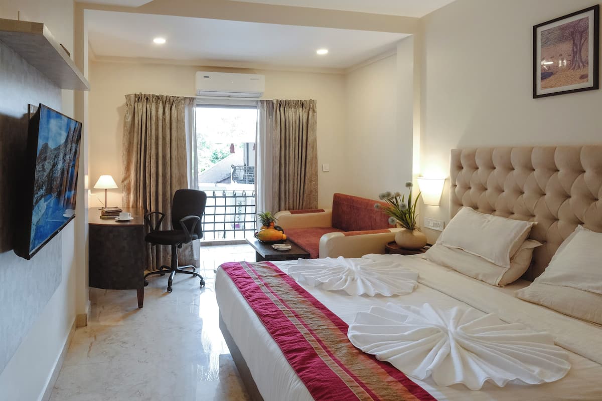 A hotel room with a bed, a desk, a chair, a sofa, and a TV.