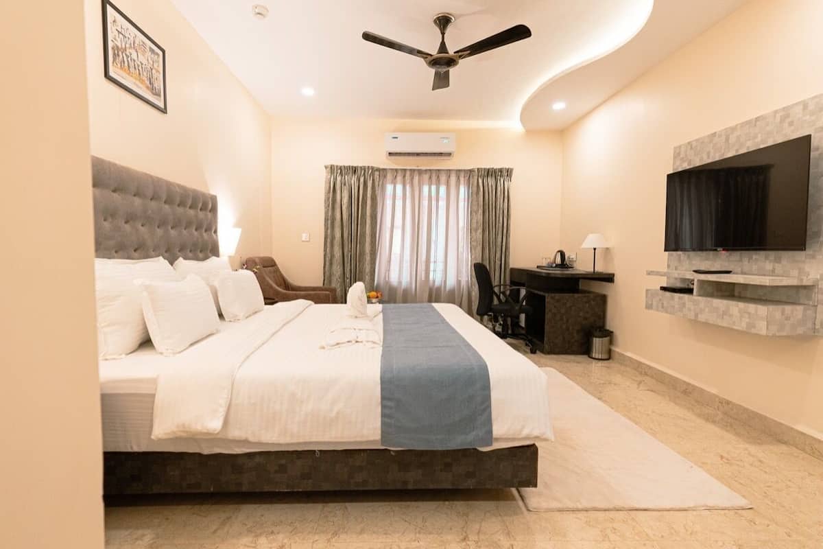 A bedroom with a bed, a desk, a chair, a television, and an air conditioning unit.