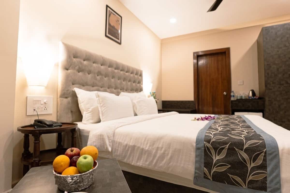 A hotel room with a large bed, a bedside table with a phone, a fruit bowl, and a wardrobe.