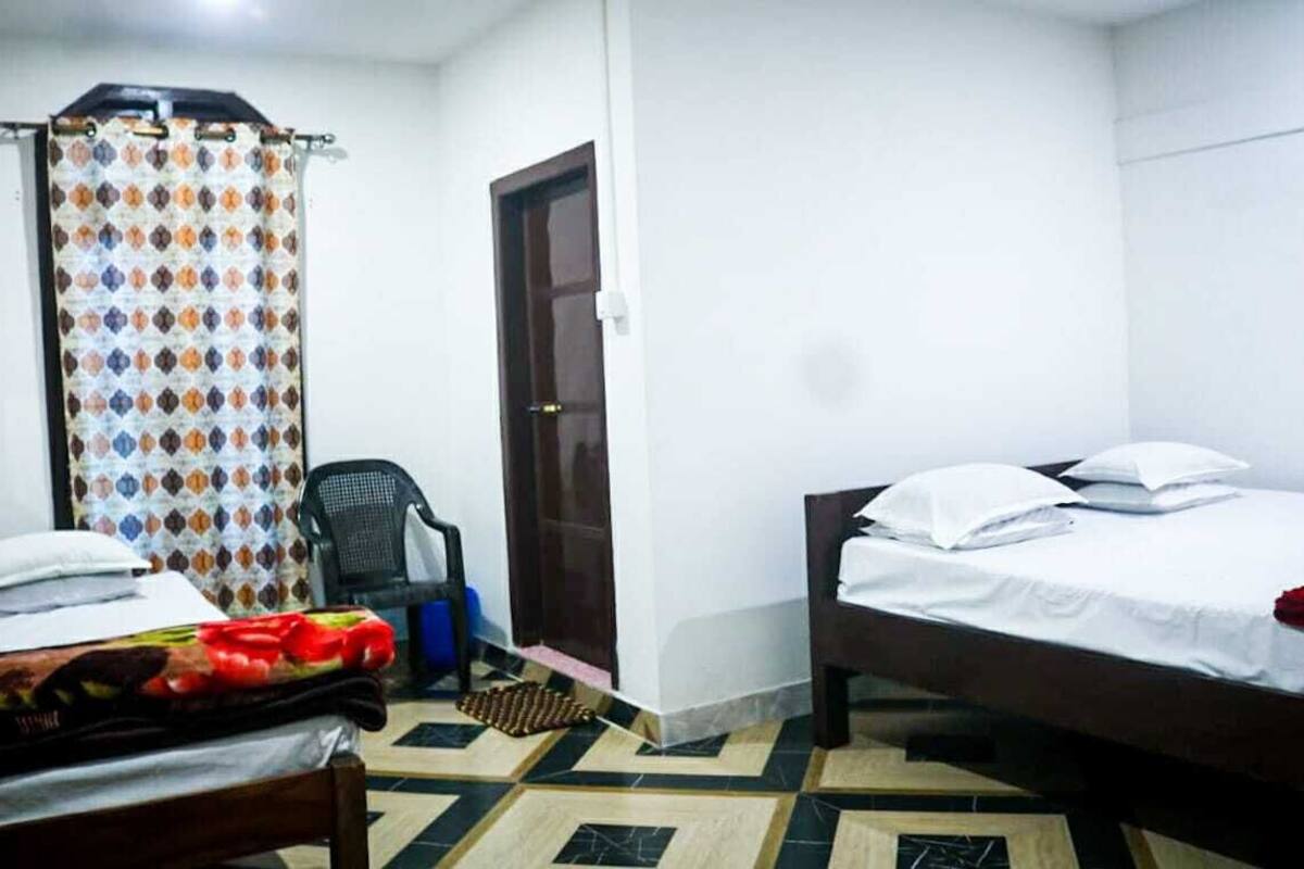 A room with two beds, a shower curtain, a door, and a chair.