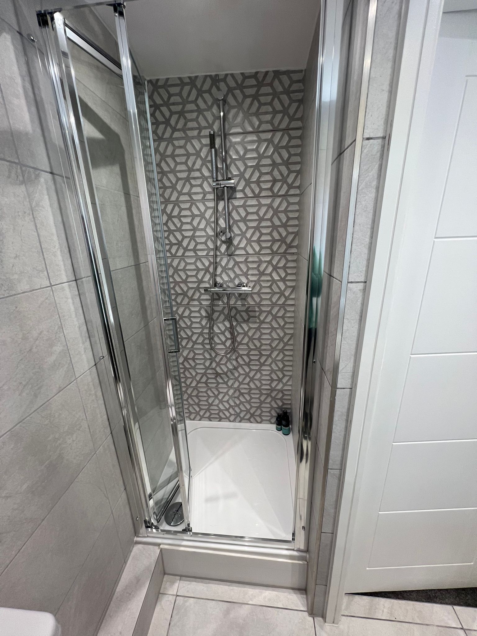 A modern shower room with a glass door, a showerhead, and a tiled wall with a geometric pattern.