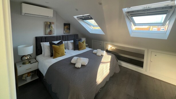 Un dormitorio moderno con una cama grande, tragaluces, una mesita de noche con lámpara y obras de arte en las paredes.