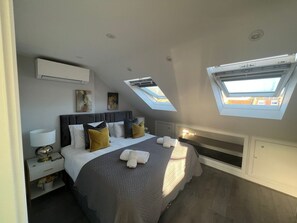 A modern bedroom with a large bed, skylights, a bedside table with a lamp, and artwork on the walls.