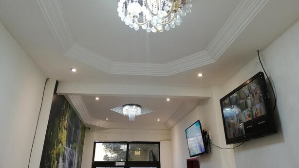 A room with a chandelier, recessed ceiling lights, a large window, and a flat-screen TV mounted on the wall. - Defountain Guest house (Johannesburg)