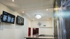 A hotel reception area with a digital screen displaying room information, a chandelier, and a waterfall mural. - Defountain Guest house (Johannesburg)