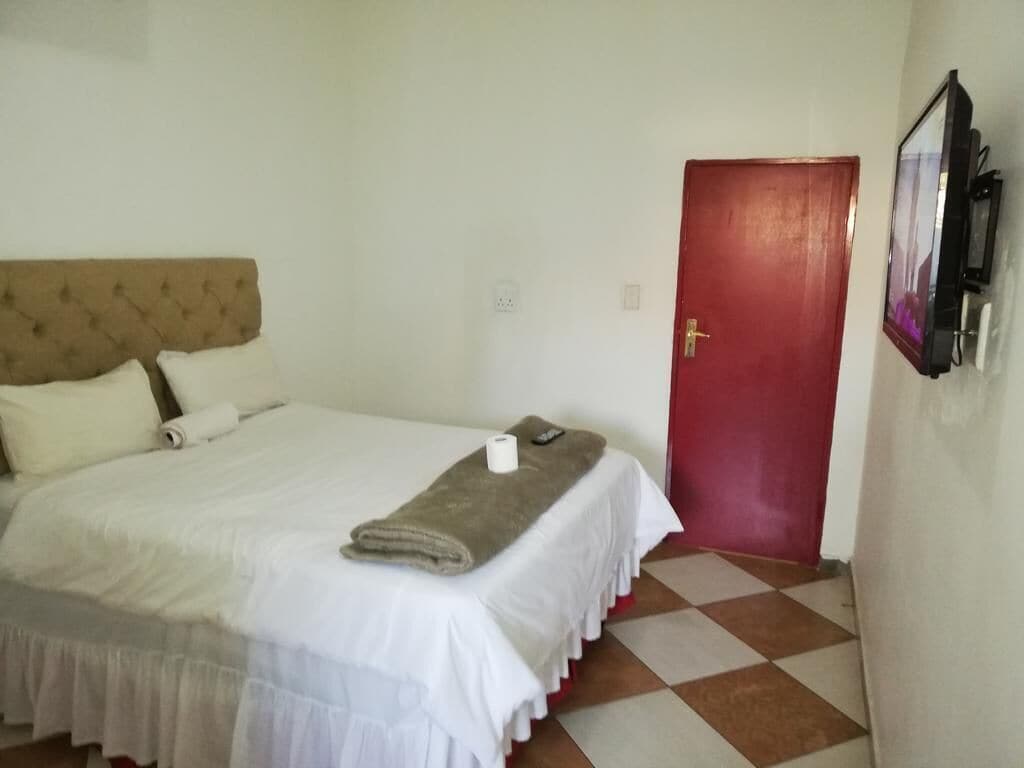 A hotel room with a bed, a red door, and a wall-mounted TV.