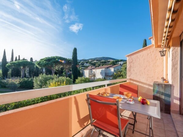 Un balcón con una mesa y una silla, con vistas a un paisaje pintoresco con árboles y casas.