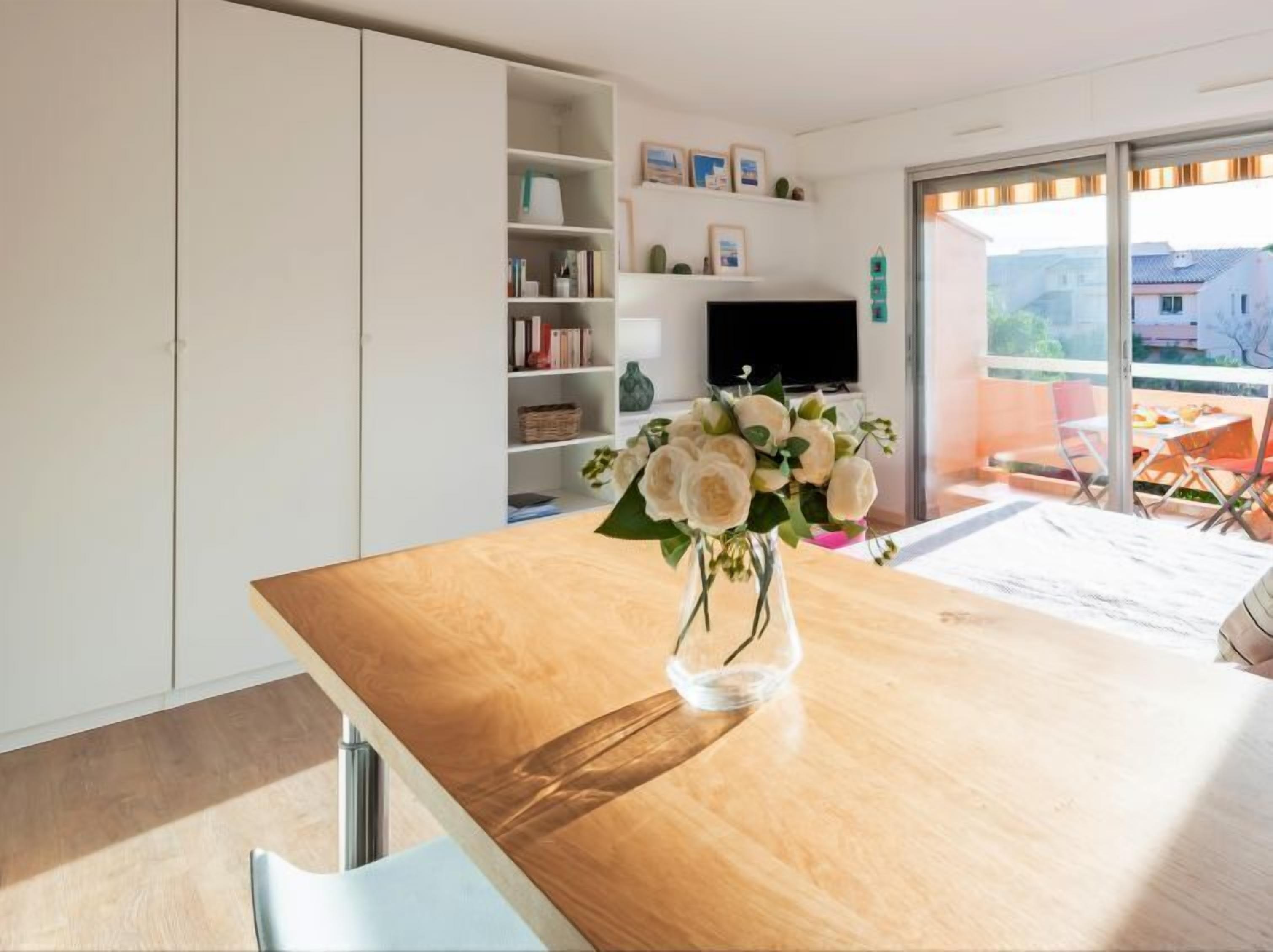A modern kitchen with a wooden countertop, a vase with flowers, and a dining area with a table and chairs.