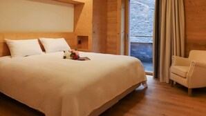 Ein Schlafzimmer mit einem großen Bett, einem hölzernen Kopfteil, einem Sessel und Blick durch eine Glastür.