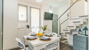 Une cuisine moderne avec des meubles blancs, une table à manger pour quatre personnes et un escalier menant à l’étage supérieur.