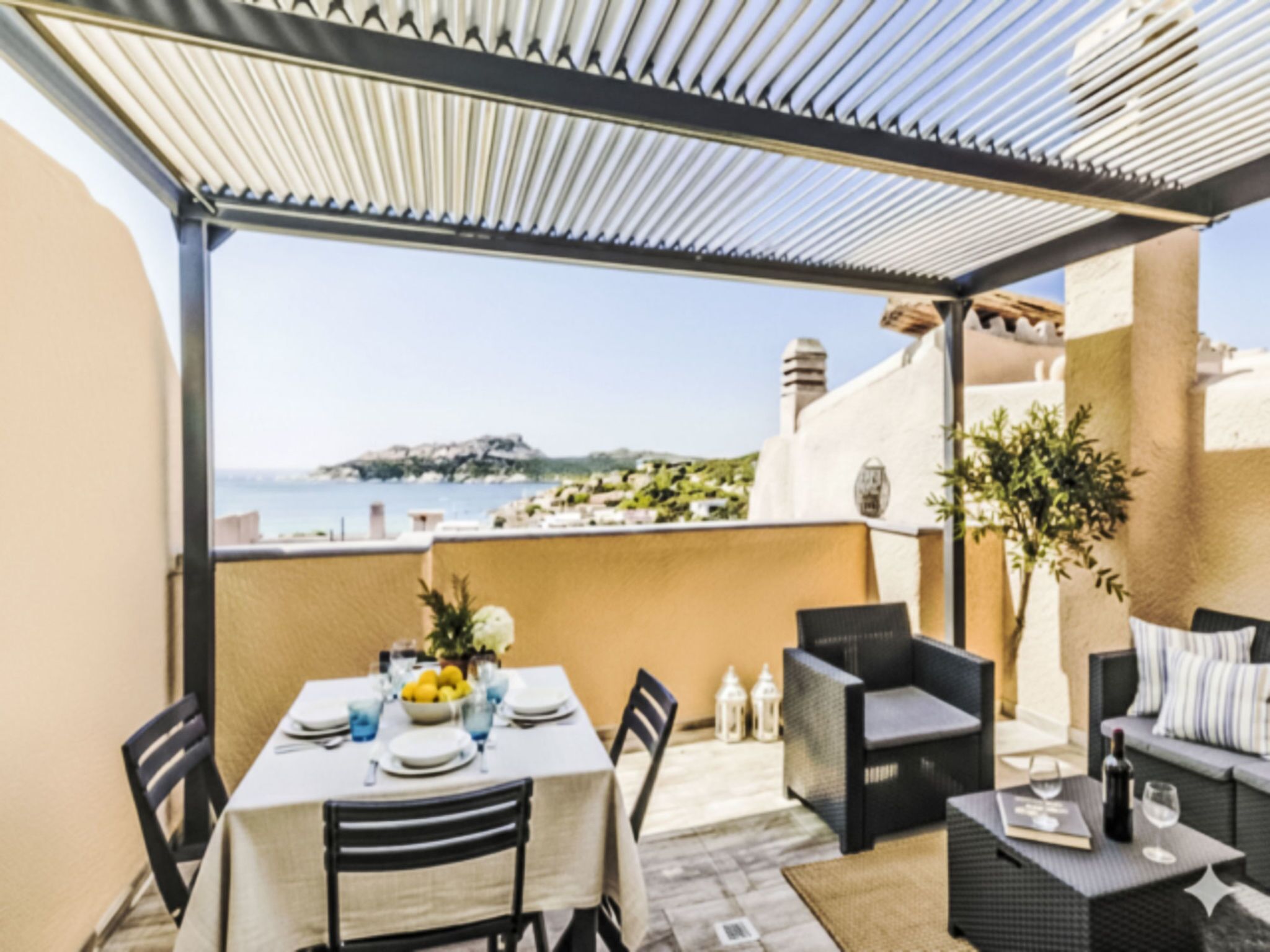 A terrace with a table set for dining, outdoor seating, and a view of the sea.
