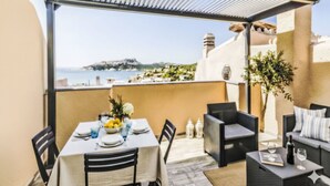 Une terrasse avec une table dressée pour le dîner, des sièges extérieurs et une vue sur la mer.