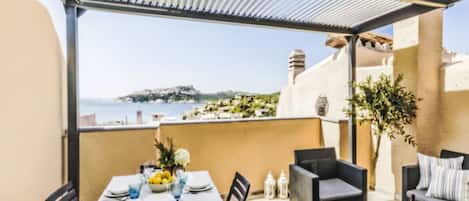 A terrace with a table set for dining, outdoor seating, and a view of the sea.