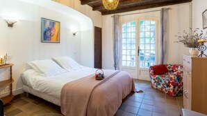 Un dormitorio con cama, una mesita de noche, una silla, una puerta con cortinas y una ventana.