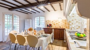 Un comedor con una mesa dispuesta para cuatro, una cocina con armarios de madera y vistas al exterior a través de grandes ventanales.